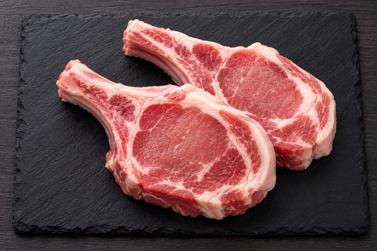 Raw pork chops on a slate board with herbs and spices