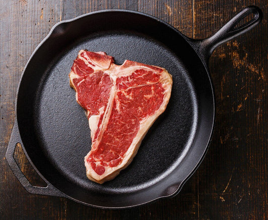 Raw steak on a cast iron skillet on a wooden surface