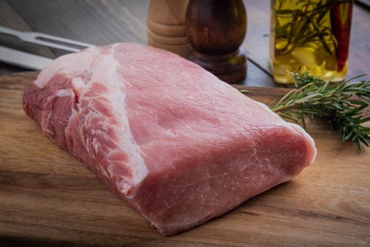 Raw pork shoulder on a wooden cutting board with rosemary and olive oil.