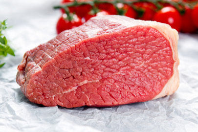Raw beef steak on a white paper with cherry tomatoes and herbs in the background