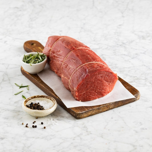 Raw beef on a wooden cutting board with seasonings on a light marble background