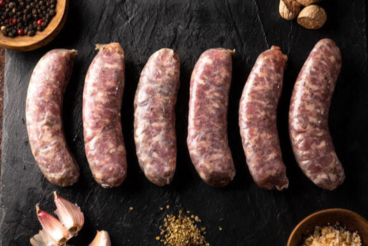 Raw sausages on a dark slate surface with garlic, spices, and nuts.