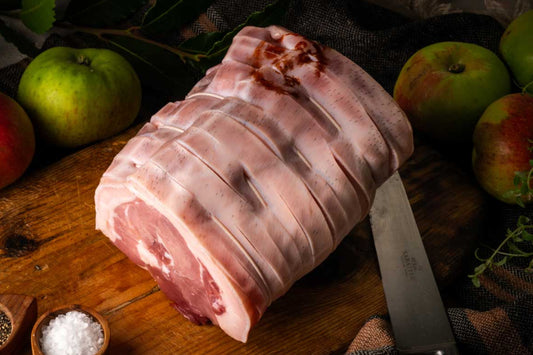 Raw bacon wrapped meat on a wooden cutting board with apples and herbs