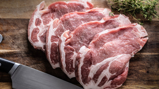 Raw meat slices on a wooden cutting board with a knife and herbs.