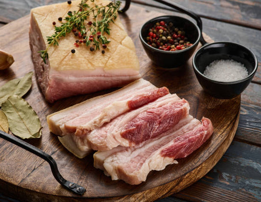 Raw pork belly on a wooden cutting board with spices and seasonings.