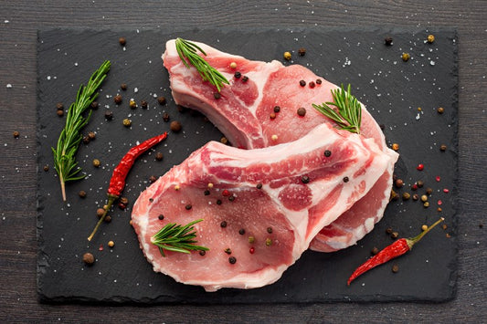 Raw pork chops on a slate board with herbs and spices