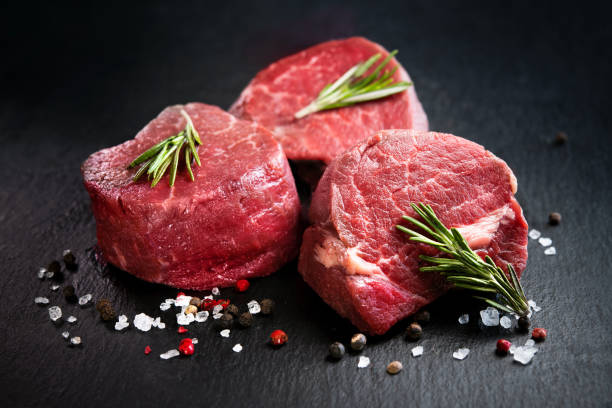 Raw beef steaks with rosemary on a dark surface