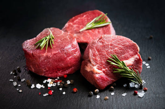 Raw beef steaks with rosemary on a dark surface