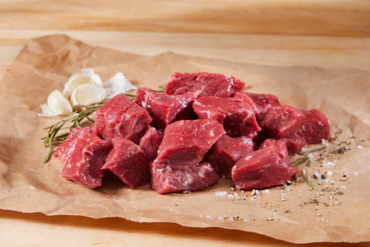 Raw beef cubes on brown paper with garlic and rosemary on a wooden surface