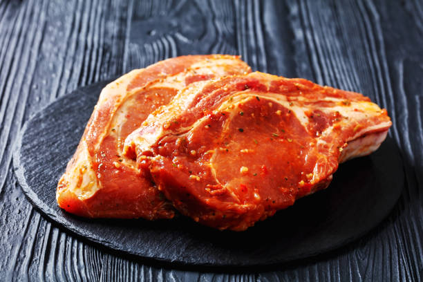 Two pieces of raw meat on a dark slate surface with a wooden background