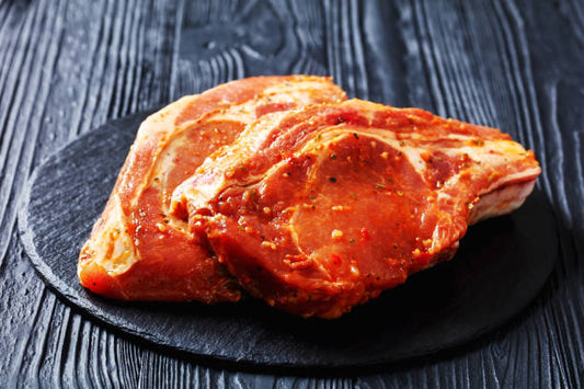 Two pieces of raw meat on a dark slate surface with a wooden background